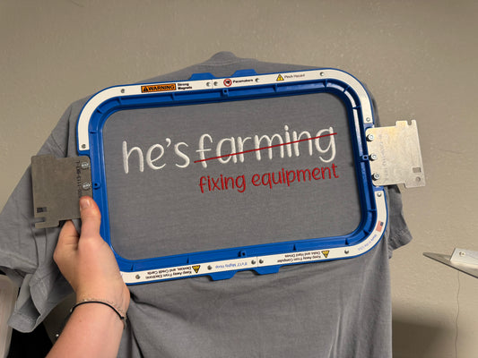 “He’s Farming… Fixing Equipment” Embroidered T-Shirt